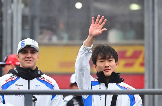 Yuki Tsunoda waves to the crowd next to his team-mate Isack Hadjar