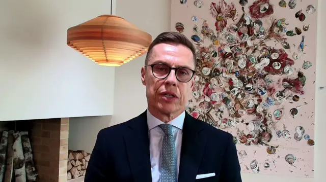 Finnish President Alexander Stubb, wearing a suit and blue tie with glasses, speaking.