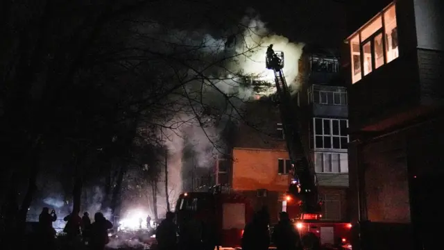 Firefighters at the site of an apartment building hit by a Russian drone strike. Smoke can be seen billowing out of the apartment