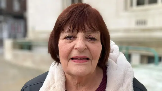 Hazel Simmons stood outside Luton town hall. She has brown hair and is wearing a fur-lined waterproof coat and dark red jumper. She is looking directly at the camera.