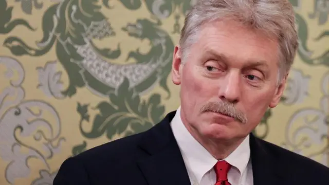 Dmitry Peskov in front of some wallpaper with a dragon on it.