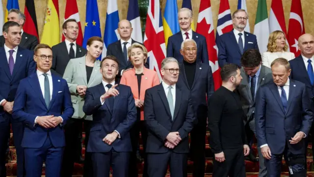 A family photo of global leaders wearing formalwear. Macron, Starmer and Zelensky are standing in the front.