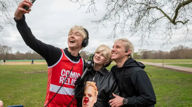 Sam and Danni in blonde wigs, posing for a photo with Jamie before he set off for his challenge