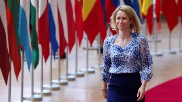 Kaja Kallas, the EU's foreign policy chief, walking on a red carpet with several flags in the background.