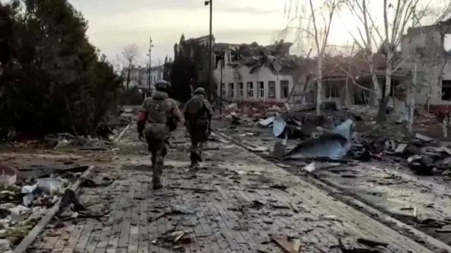 Russian service members walk past a destroyed building in the town of Sudzha in Kursk, which was recently retaken by Russia's armed forces - pictured from the Russian Defence Ministry