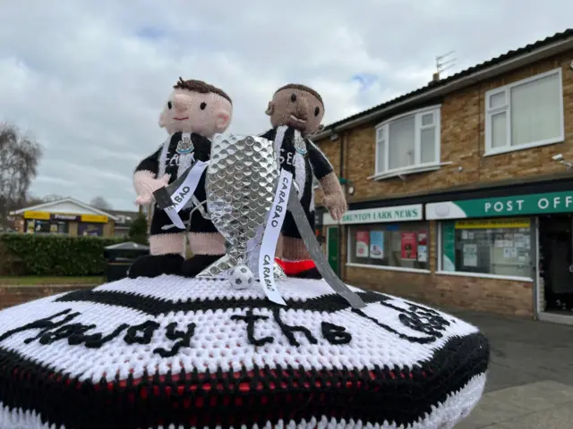 A post box with a knitted topper of Newcastle players winning the Carabao Cup