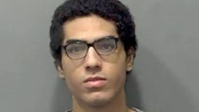 Custody mugshot of Nicholas Prosper, who is wearing black glasses and has black hair. He has a serious expression on his face.