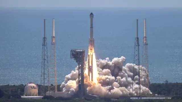 The initial stage of the rocket launch - a fiery jet blasts from the base, with smoke shooting out and covering the coastal landscape