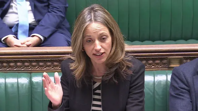 Helen Whately speaking in the Commons. She raises her hand while she makes her point, and the green benches and other MPs are visible behind her