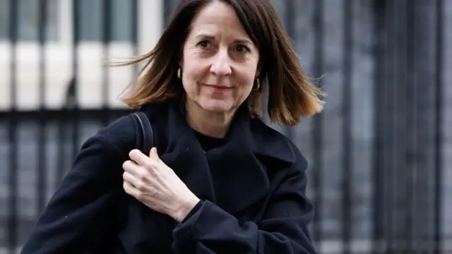 Liz Kendall, a woman with brown hair in a black coat, walks down Downing Street with a hand holding her bag