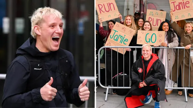 Jamie Laing smiling with thumbs up and posing in front of an audience holding encouraging placards