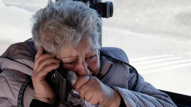 A woman looks distressed as she speaks on the phone, covering her mouth with her hand.