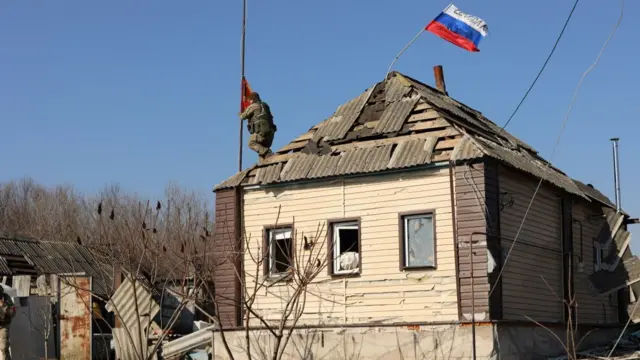 A Russian service member places a flag on the roof of a house in a part of the Kursk region, which was recently retaken by the Russian Armed Forces