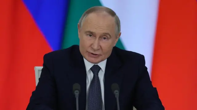 Putin speaks behind a microphone wearing a suit.