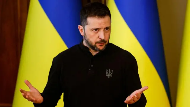 Zelensky gestures while he speaks, wearing a black top.