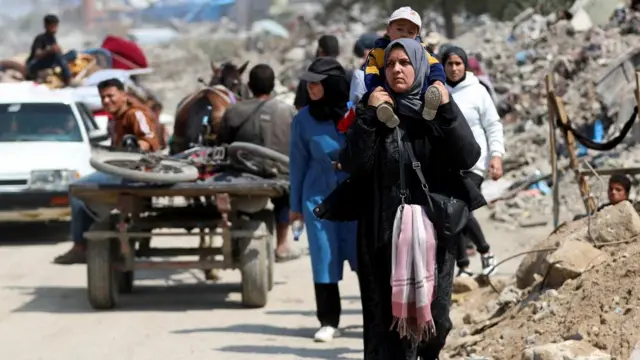 A woman holding a boy on her shoulders and other people walking behind her