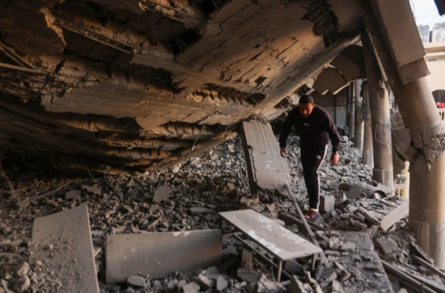 A man walks through the rubble of a destroyed section of a school-turned-camp following an Israeli strike in Gaza City on 18 March 2025