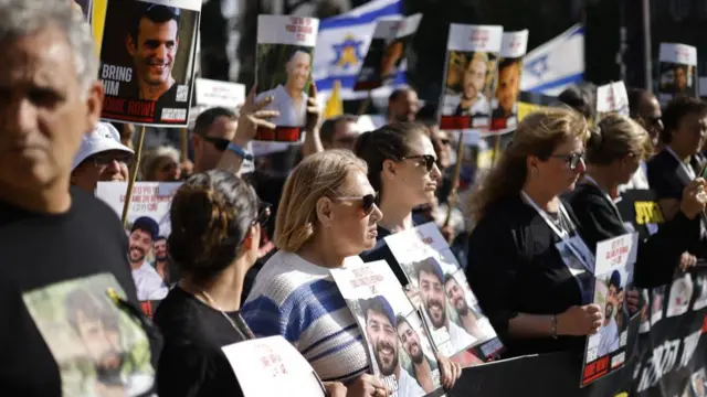 Family members and supporters of hostages stand outside the Knesset holding banners with pictures of hostages