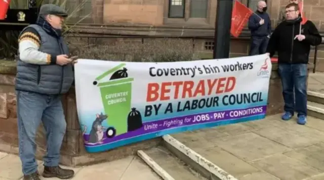 Two men in coats and jeans with a large banner which reads Betrayed by a Labour Council