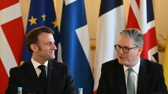 Macron smiles towards Starmer who is speaking. European flags stand in the background