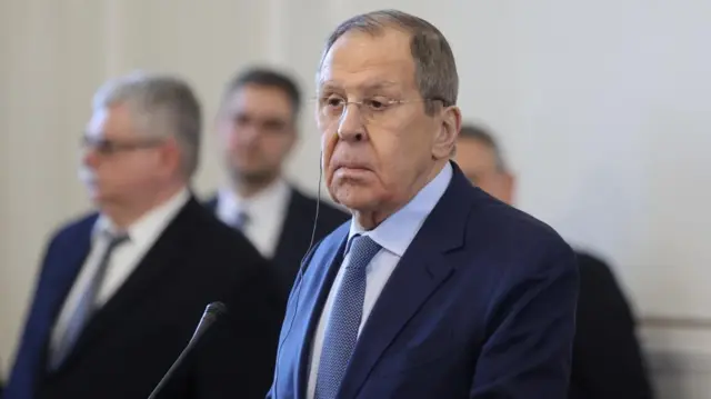 Russia Dmitry Lavrov stands at a podium with a microphone. He wears a blue suit and blue tie