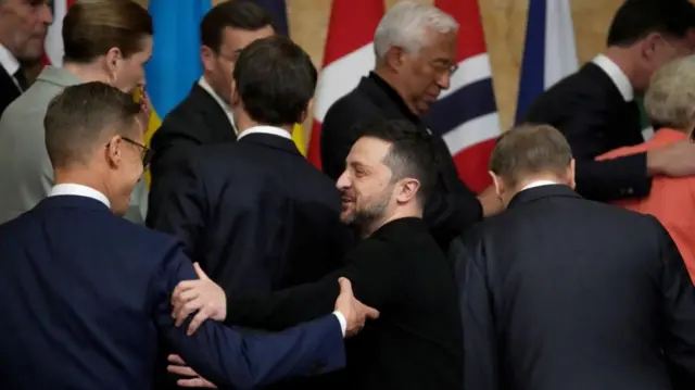 Zelensky and Finnish President Alexander Stubb grip each other's arms as other European leaders stand prepping for a group photo