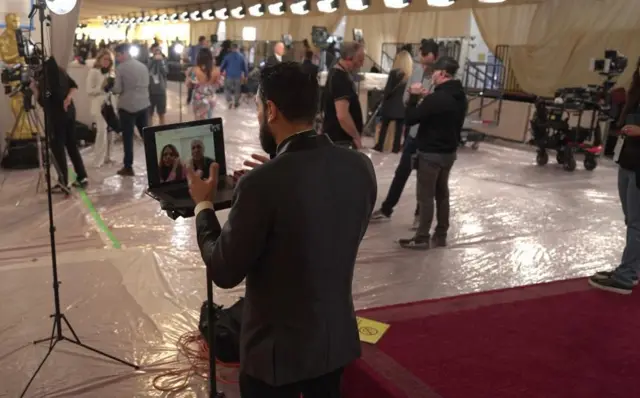 A man speaking on zoom on the Oscars red carpet