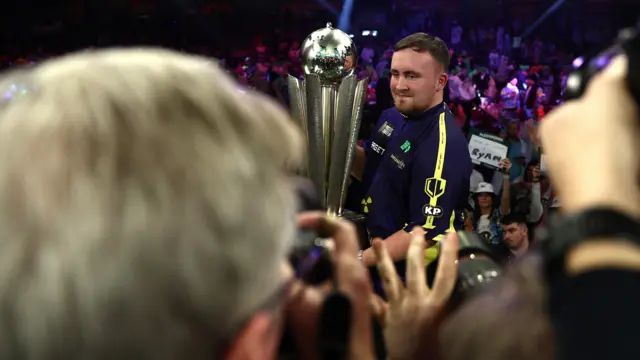 Luke Littler holds the World Championship trophy