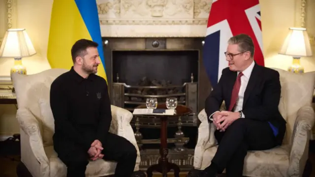 Zelensky and Starmer sit opposite one another with their respective flags draped behind them