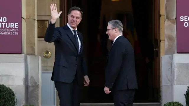 Mark Rutte waves at crowd facing camera. Keir Starmer stood next to him.