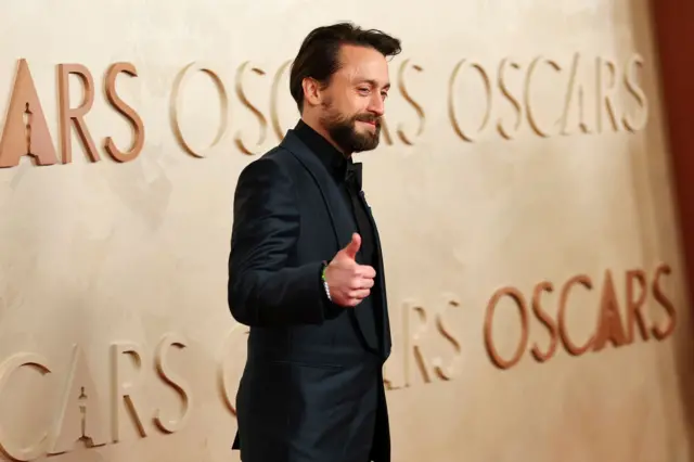 Kieran Culkin posing with a thumbs up on the Oscars red carpet