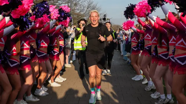 The Loughborough Students Cheerleading team have pom poms and are cheering Jamie over the line