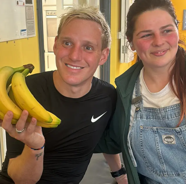 Jamie Laing holding a bunch of bananas while sitting on a massage table