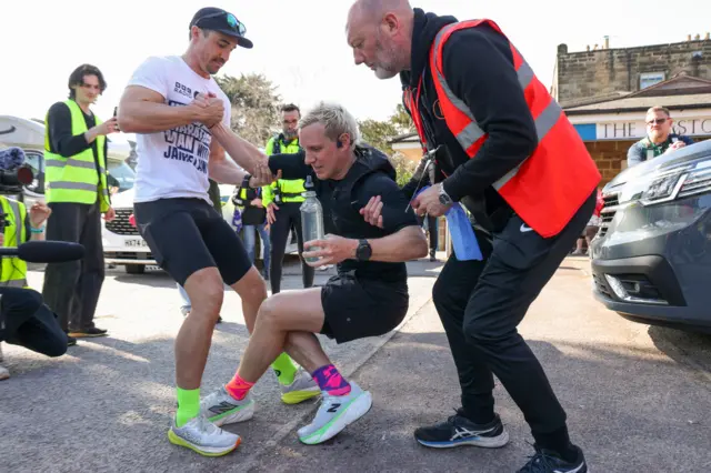 Jamie is helped up by two of his team