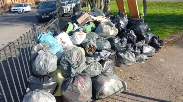 A large pile of bin bags propped up against black metal railings.