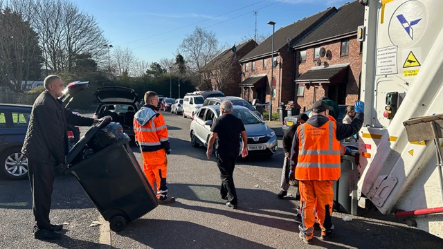 People queue up to dispose rubbish at a bin lorry, with line of houses on the right