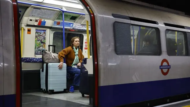 A woman holds her suitcase in place on a London tube carriage