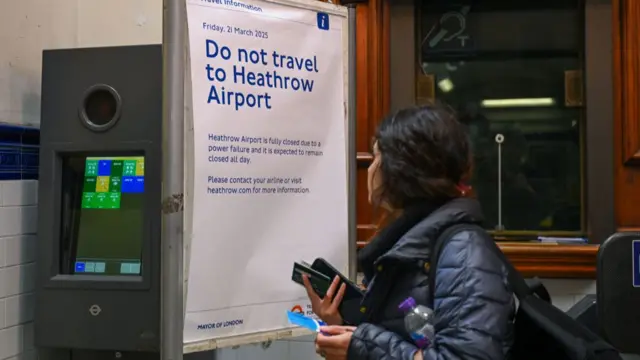 A woman looks at a sign advising passengers not to travel to Heathrow airport