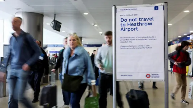 People walk at the Paddington railway station. A sign in the foreground warns against travel to Heathrow.