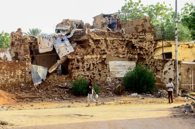 A Sudanese boy looks on as a woman walks past a damaged building in Khartoum's twin-city Omdurman