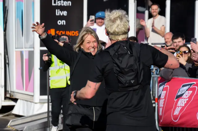 Jamie's mum smiling with her arms outstretched as Jamie runs to the finish line