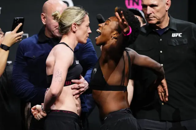 Molly McCann stands with her hands behind her back as Alexia Thainara shouts in her face at a UFC weigh-in