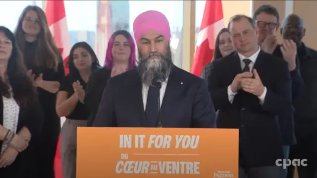 NDP leader Jagmeet Singh stands behind a podium surrounded by supporters.