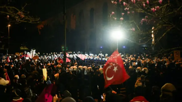 Protestors holding Turkish flags stand in front of Turkish anti-riot police