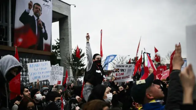 Protestors hold signs and Turkish flags during a rally in support of Istanbul's arrested mayor at Istanbul's city hall, on March 24, 2025