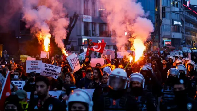 Escorted by riot police, students burn flares as they walk