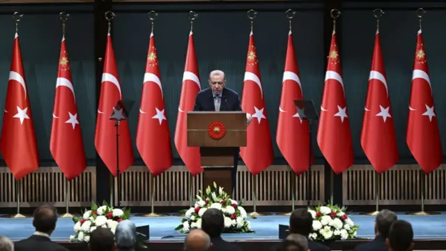 Turkish President Recep Tayyip Erdogan presents statements in front of a line of Turkish flags