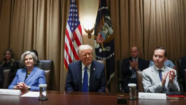 Donald Trump winks as he sits next to colleagues at a long table in the White House.