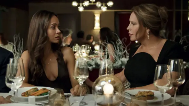 Zoe Saldana's character sat at a dinner table with Emilia Perez  with fine dining and wine surrounding them