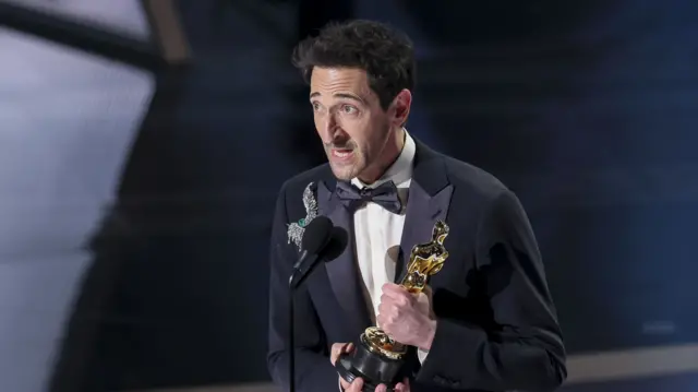 Adrien Brody giving his acceptance speech on stage, while holding an Oscar.